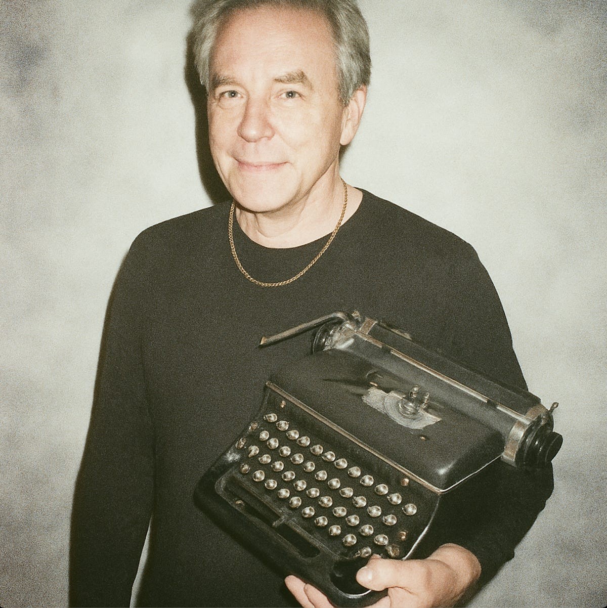 Bernd Best, author wearing a gold necklace and holding a typewriter